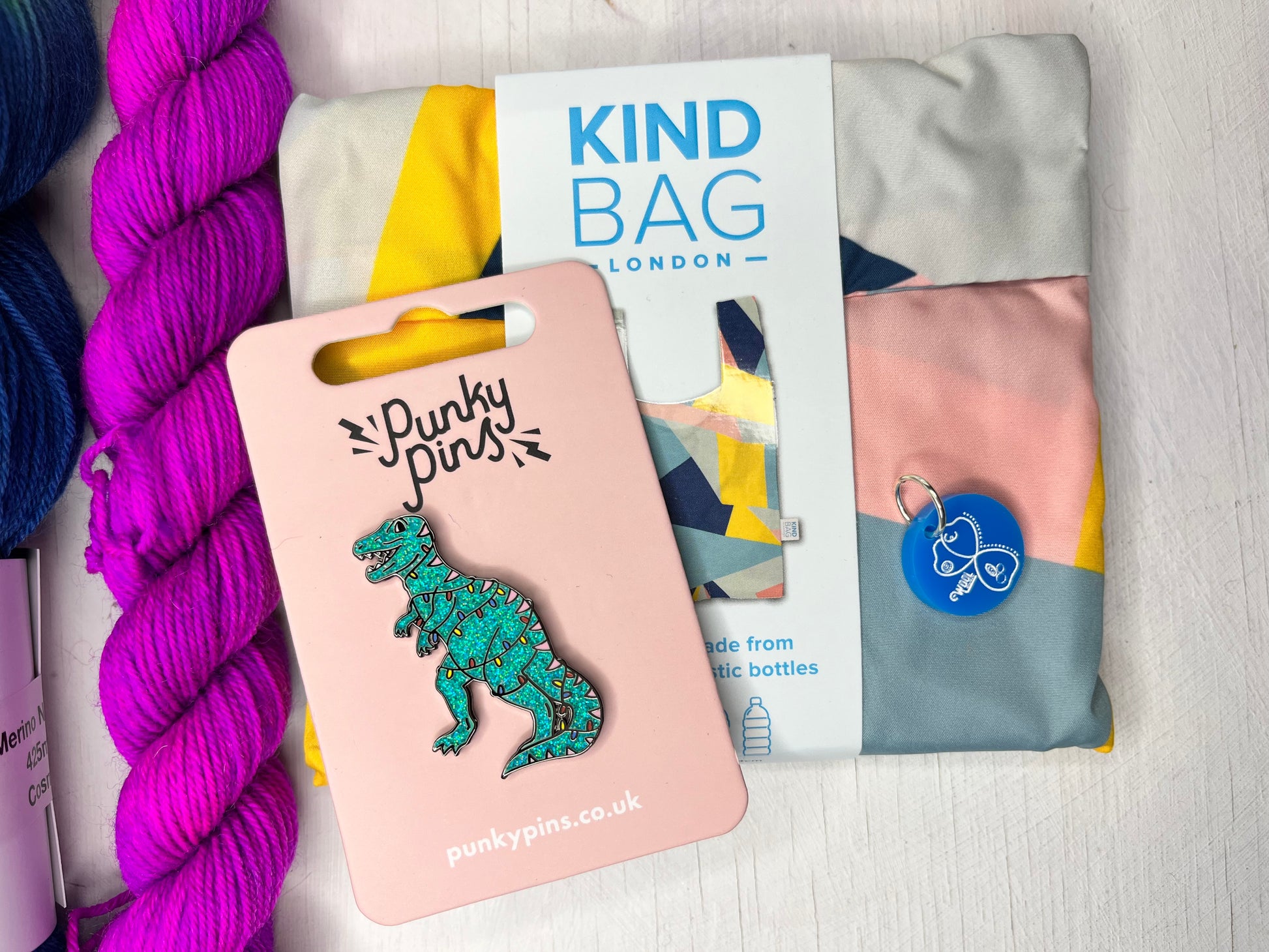 Punky Pins dinosaur enamel pin on a pink card with Kind Bag London mini bag in the background and a stitch marker